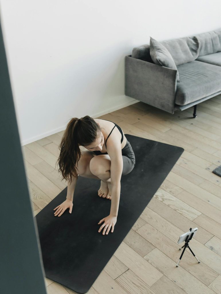 Young woman practicing yoga indoors, using a smartphone tripod to record her session.